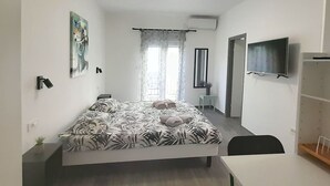 Een slaapkamer met een bed, een bureau, een stoel, een televisie, een kledingkast en een raam met gordijnen.