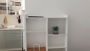 Een eethoek met een witte tafel en zwarte stoelen, een witte boekenkast met een plant en een wandklok.