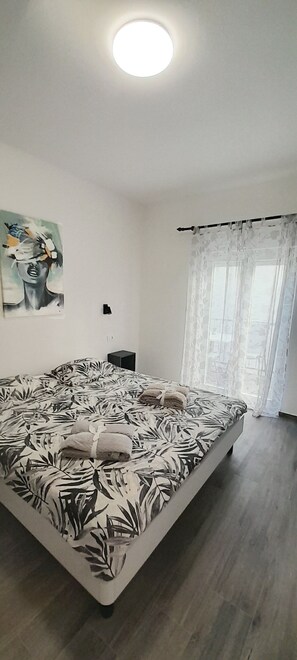 Ein Schlafzimmer mit einem großen Bett, einer Deckenlampe, einem Gemälde an der Wand und einem Fenster mit transparenten Vorhängen.