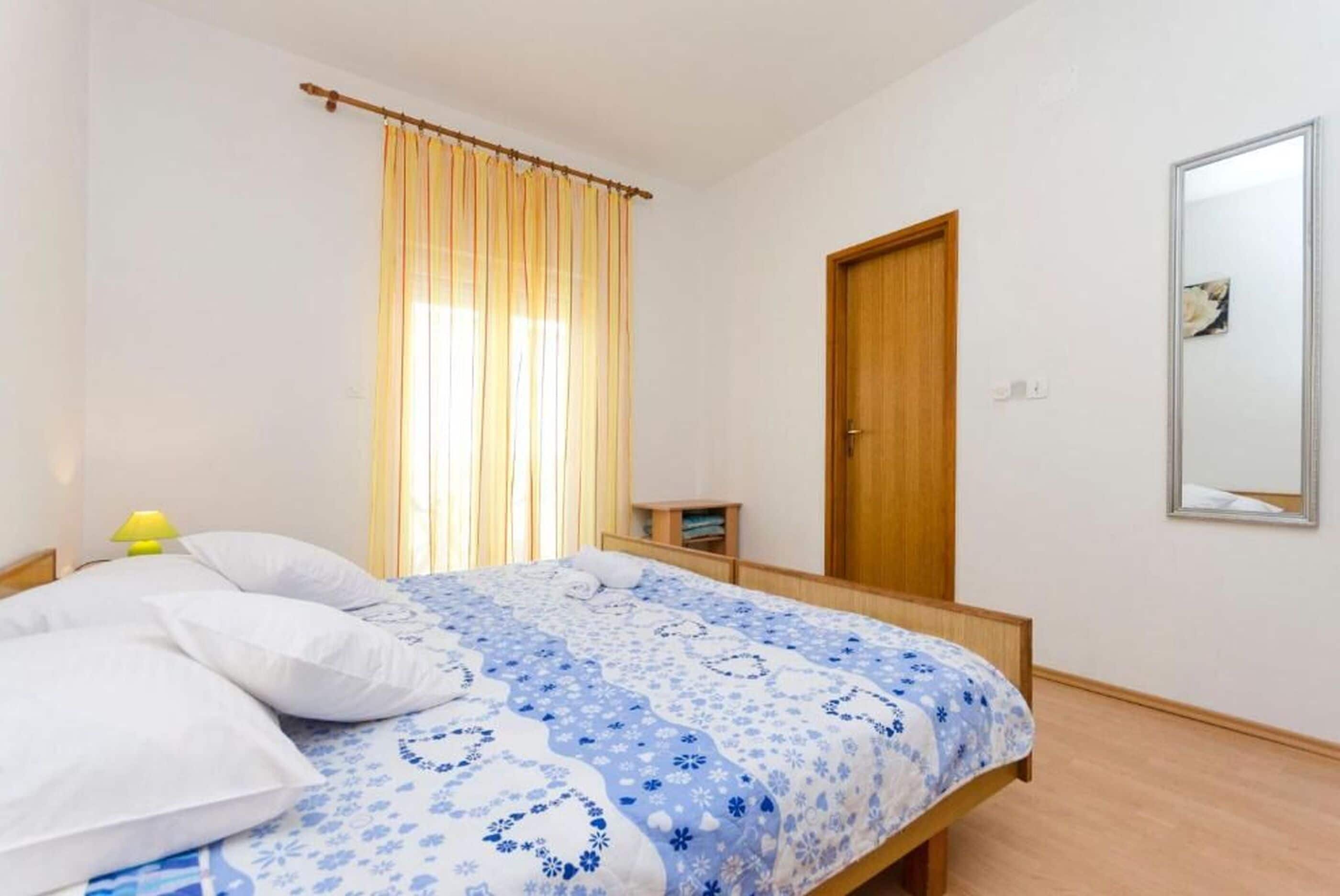 A bedroom with a bed, a wooden door, a mirror, and a window with curtains.