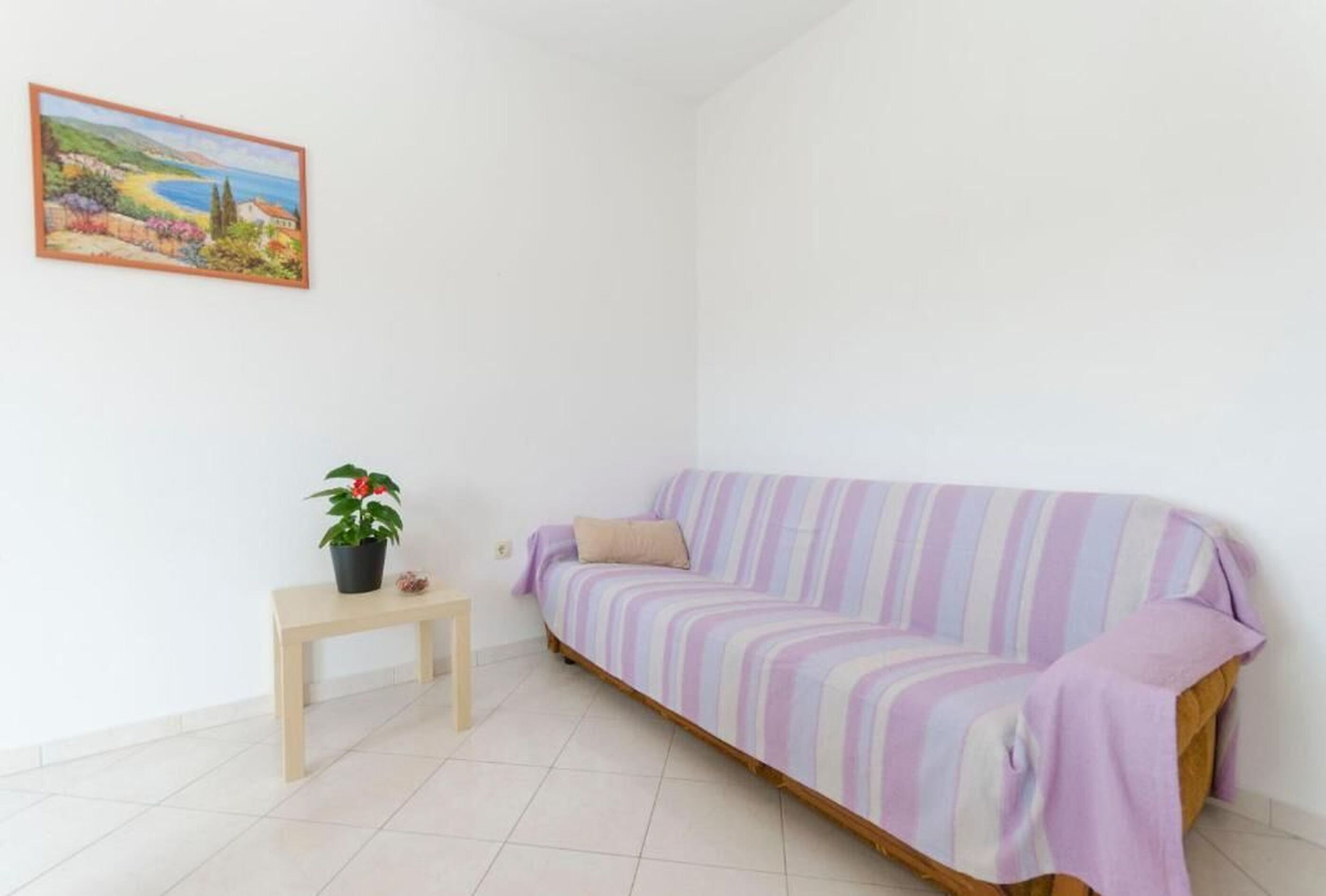 Ein Zimmer mit einem gestreiften Sofa, einem kleinen Holztisch, einem Blumentopf und einem gerahmten Gemälde an der Wand.
