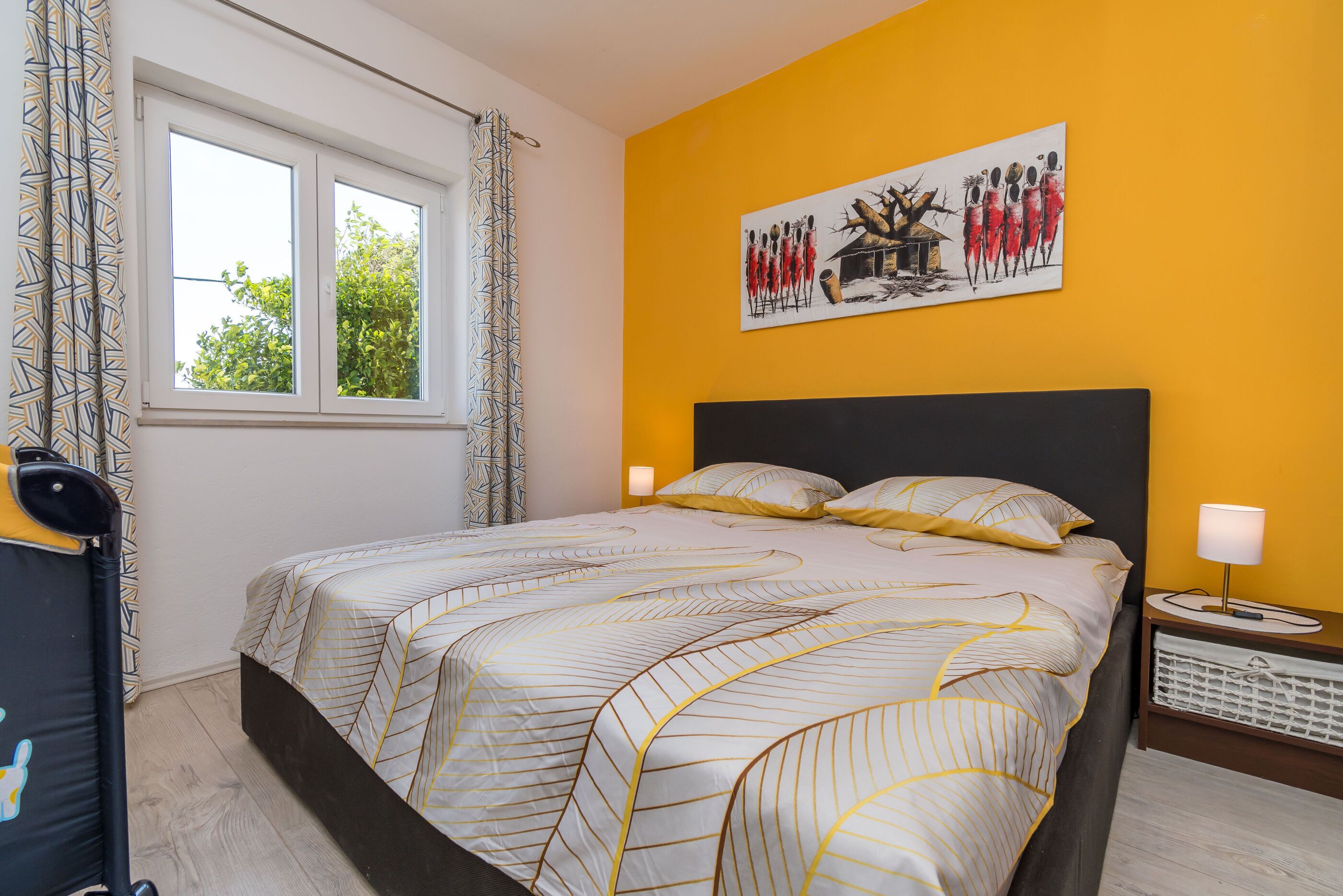 Une chambre à coucher avec un lit, une fenêtre, un tableau au mur et une table de chevet avec une lampe.