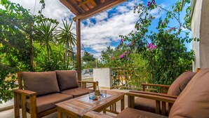 A wooden outdoor seating area with a sofa and table, surrounded by lush greenery and flowering plants. - Apartment Piveta (Okrug Gornji)