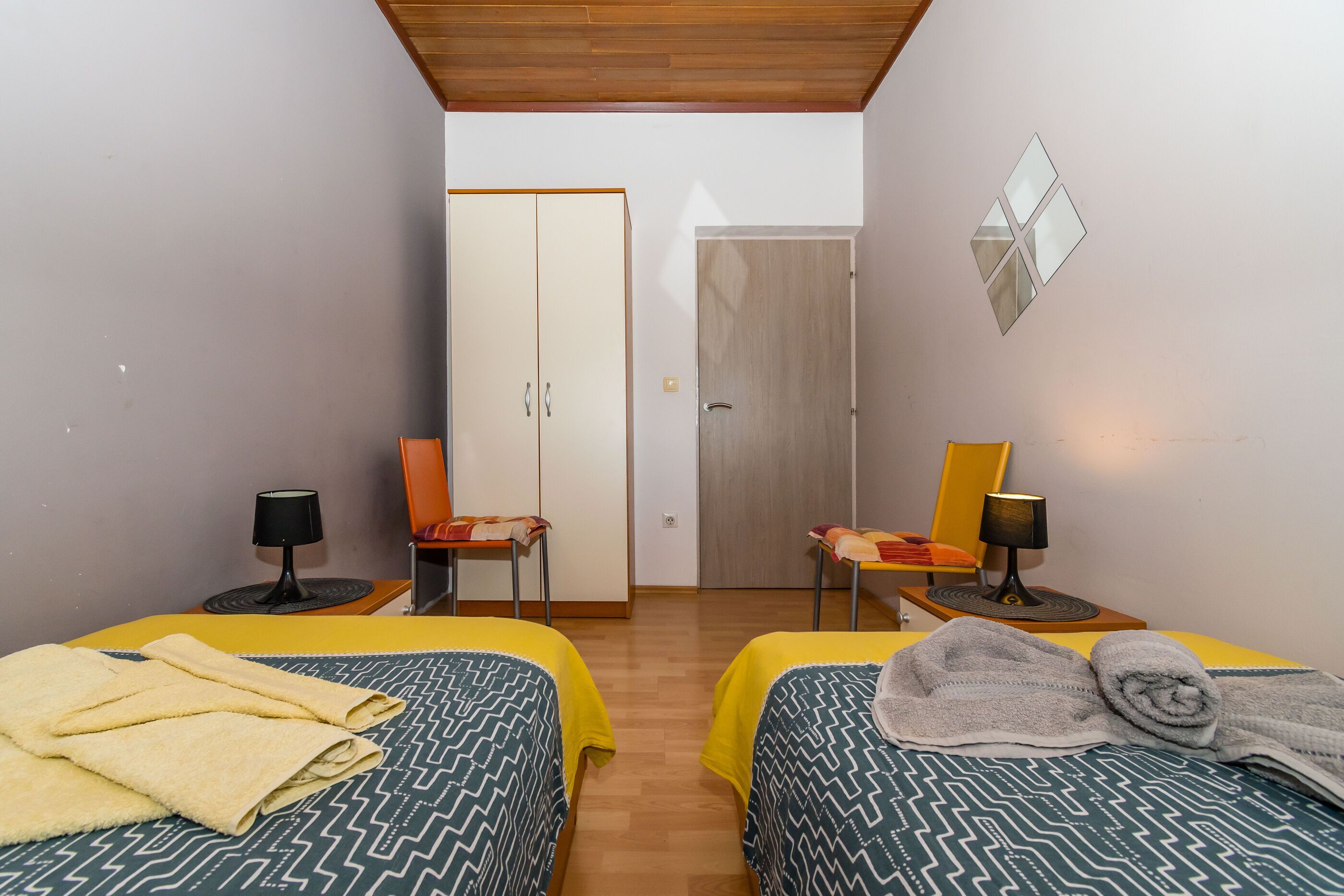 A room with two beds, a wardrobe, two chairs, and two lamps.