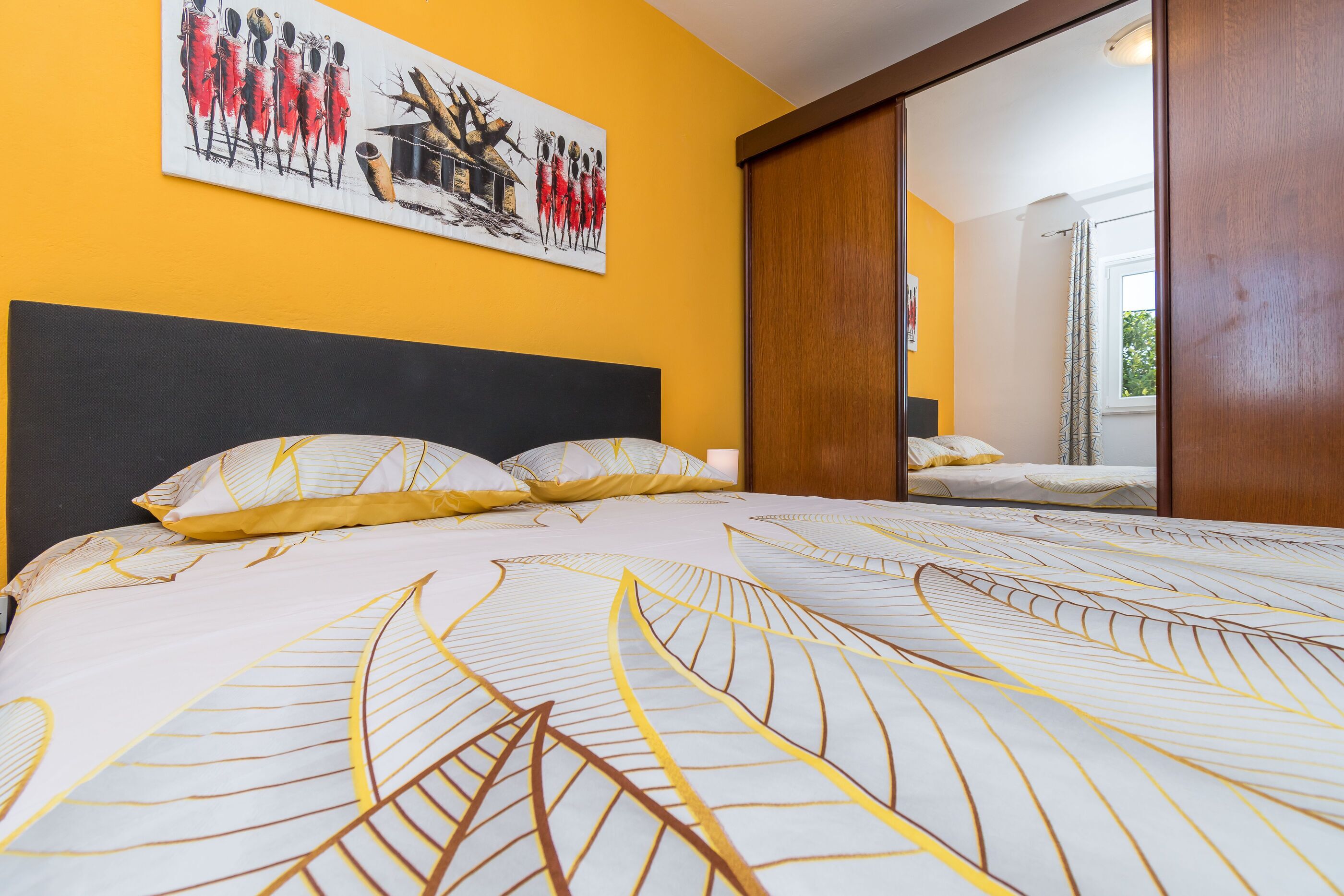A bed with a patterned bedspread, a painting on the wall, and a wooden door.