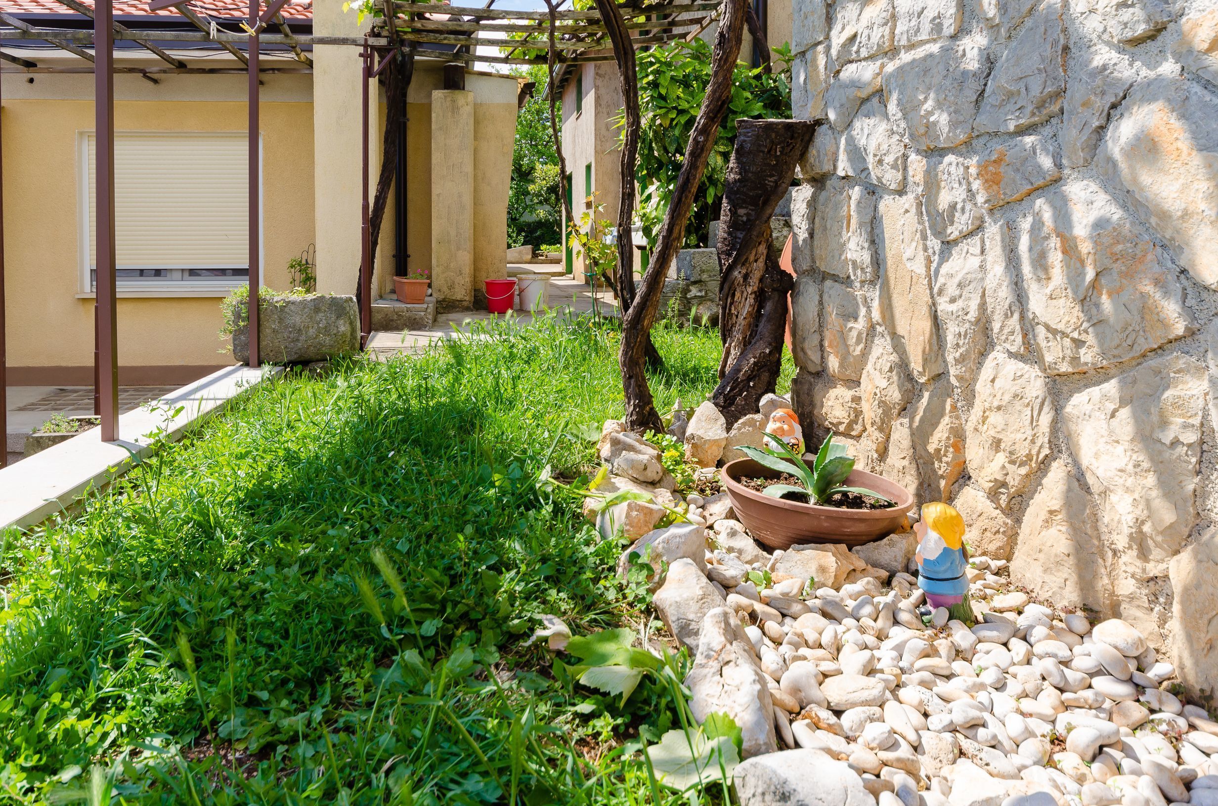 A garden area with a stone wall, a pergola, and a child playing.