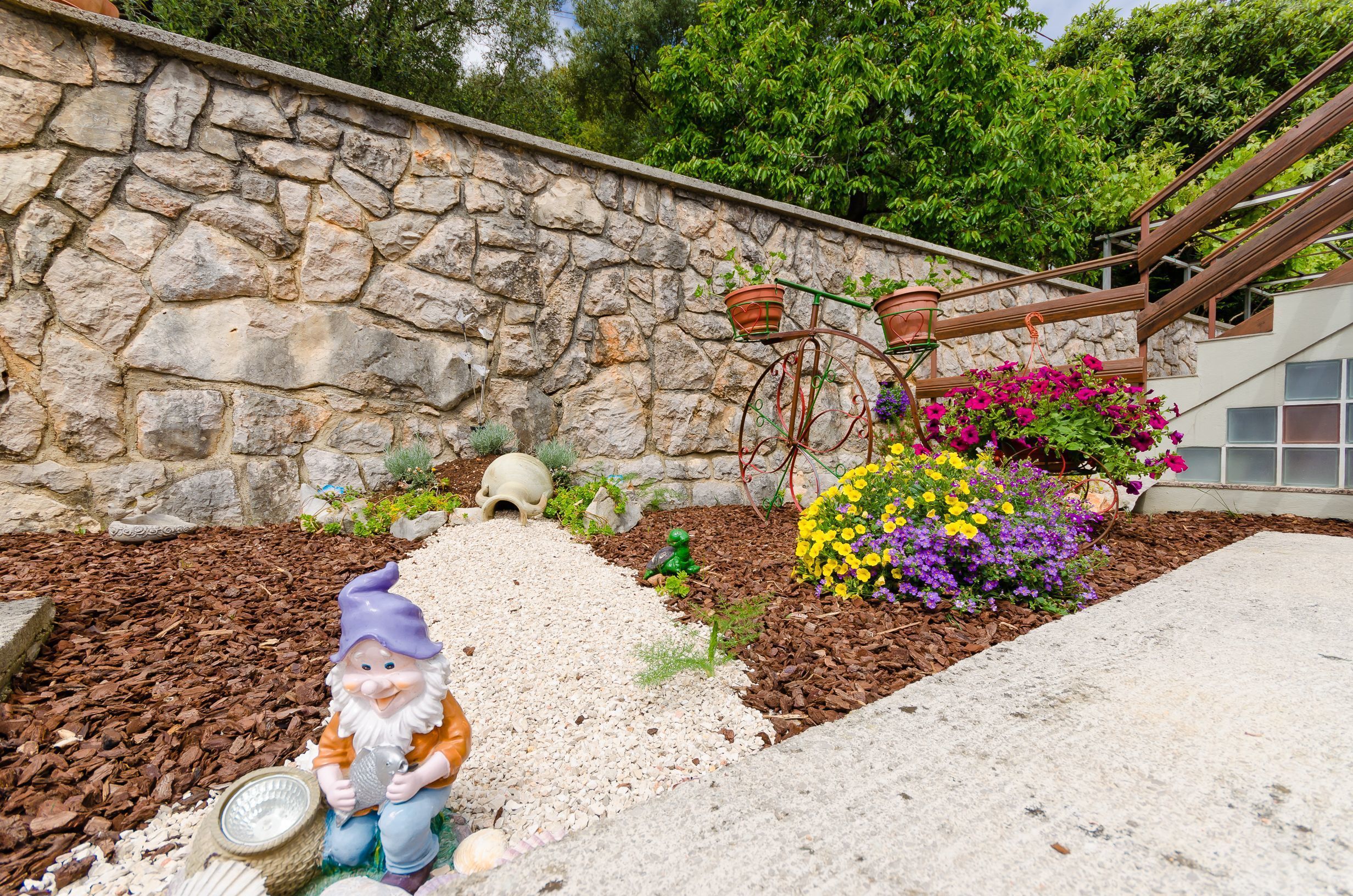 Um jardim com um muro de pedra, uma estátua de gnomo e flores coloridas.
