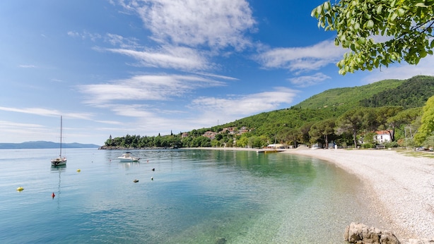 Nyilvánvaló, hogy a tengerpartról nyílik kilátás, ahol kavicsos strand, hajók és egy távoli, dombon fekvő város látható.