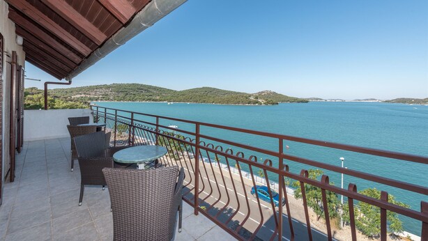 A balcony with wicker furniture, a view of a body of water, and a distant hilly landscape. - Apartment Lidija (Tisno)