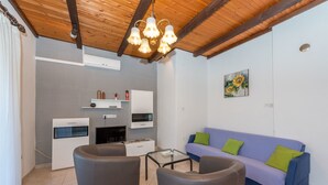 A modern living room with a wooden ceiling, a blue sofa with green cushions, and a glass coffee table. - Apartment Lidija (Tisno)