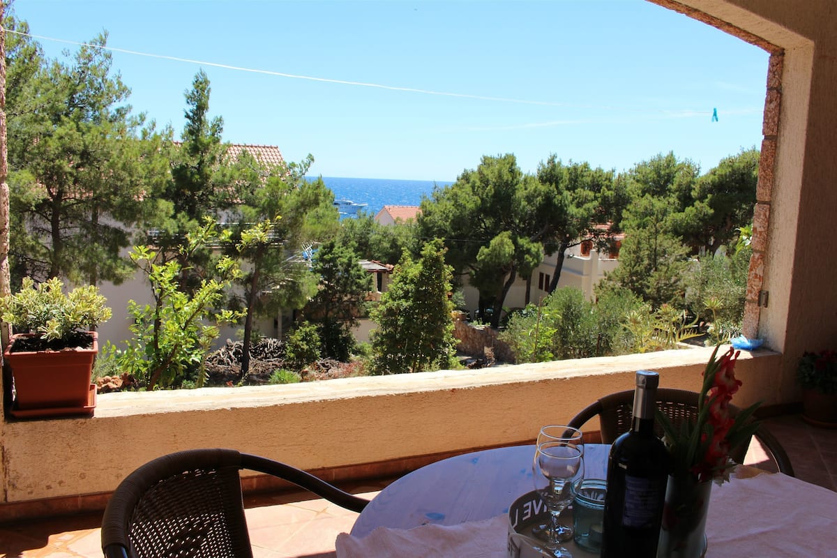 A balcony with a table, chairs, a bottle of wine, and a vase of flowers.