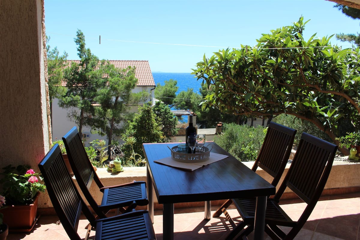 A terrace with a table and chairs, overlooking a view of the sea and buildings.