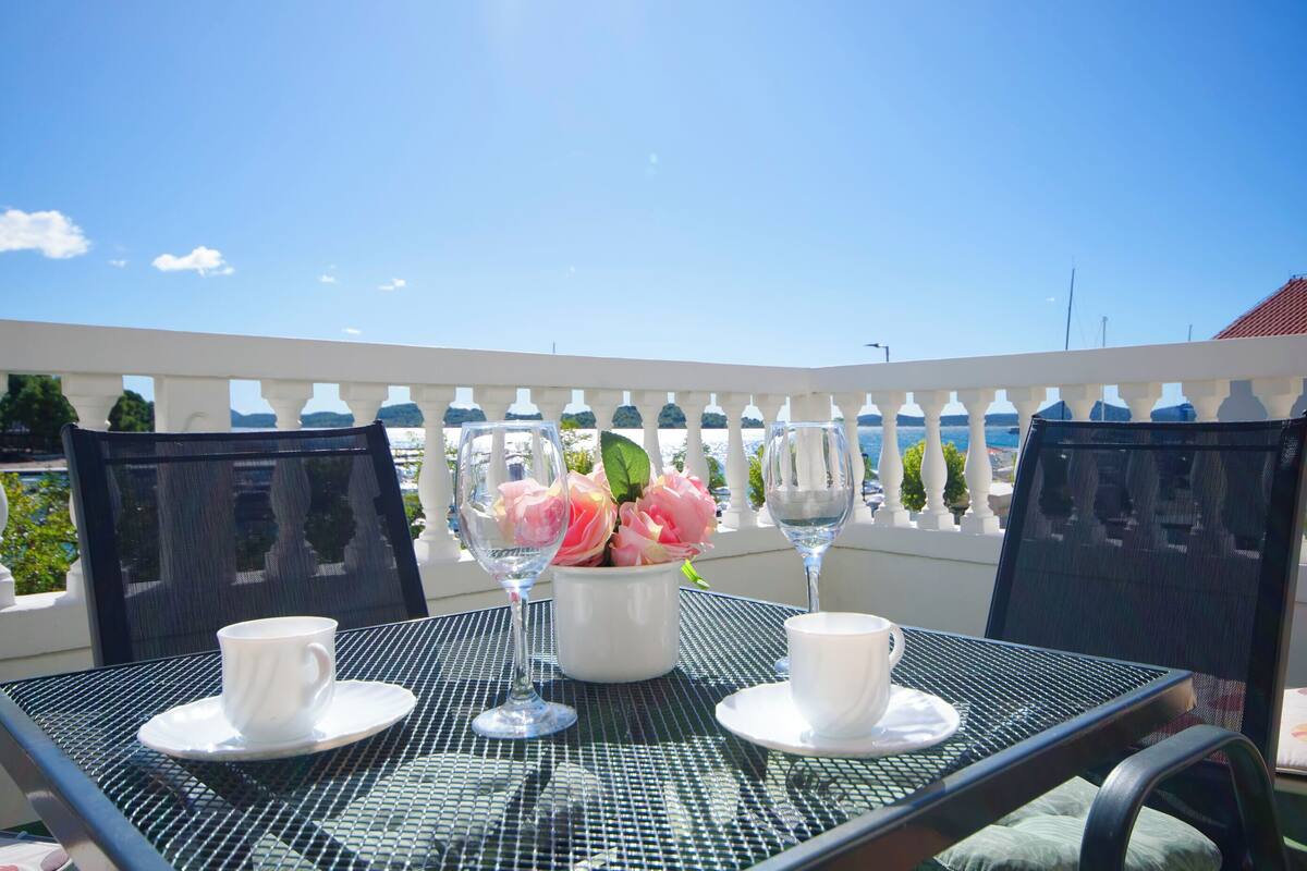 A table with two white cups and a vase of pink flowers, set against a clear blue sky.