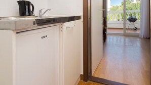 A compact kitchen with a built-in dishwasher, a coffee maker, and a sliding door leading to a balcony with a barbecue grill.