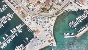 An aerial view of a marina with boats docked, a parking area, and residential buildings with red roofs.