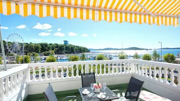 A balcony with a table set for two, overlooking a scenic view of a body of water, a Ferris wheel, and distant hills.