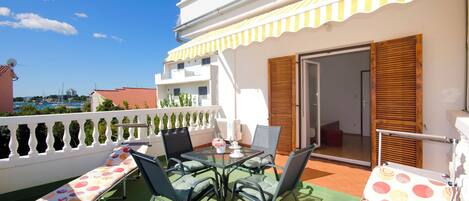 A balcony with a table and chairs, a sun lounger, and a view of the sea.