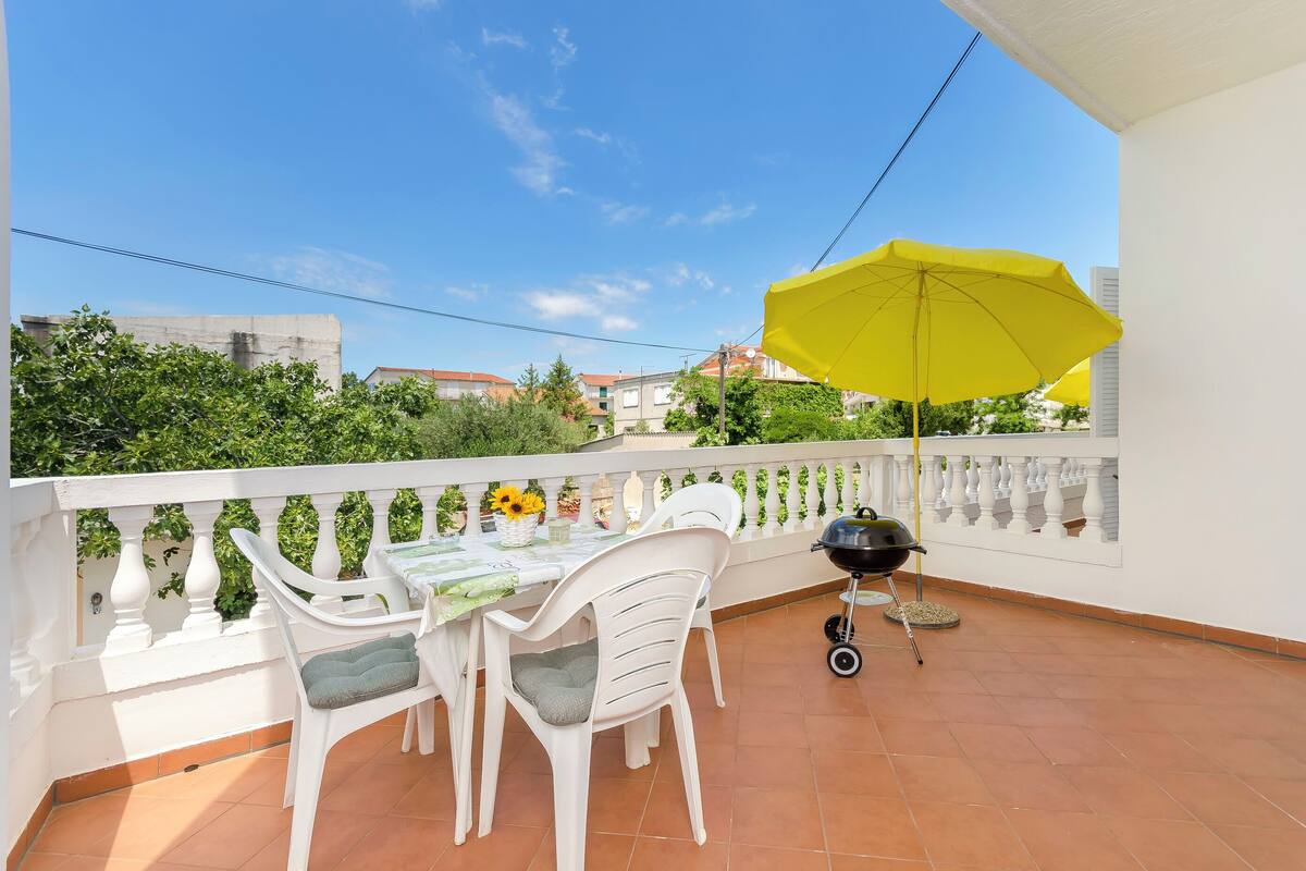 A balcony with a table, chairs, a yellow umbrella, and a grill.