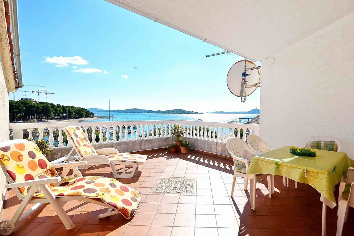 A terrace with a table and chairs, a satellite dish, and a view of the sea and distant hills.