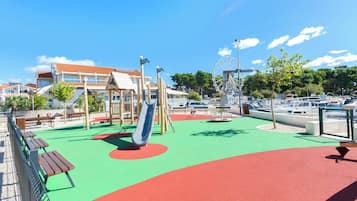 Ein Spielplatz mit Rutsche, Bänken und einem Riesenrad im Hintergrund.