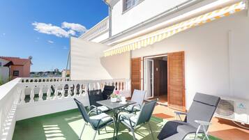 Un balcon avec une table et des chaises, une balustrade blanche et une vue sur la mer.