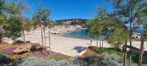 A coastal area with a pebble beach, a wooden walkway, and a view of houses on a hillside. - House Stone House in Center (Jelsa)