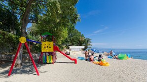 Une plage avec une aire de jeux, comprenant un toboggan et des balançoires, où les gens se détendent près de l’eau.