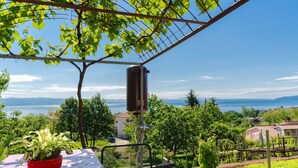 Un balcon avec une table rouge, un pot de fleurs et une vue sur un lac et des maisons.