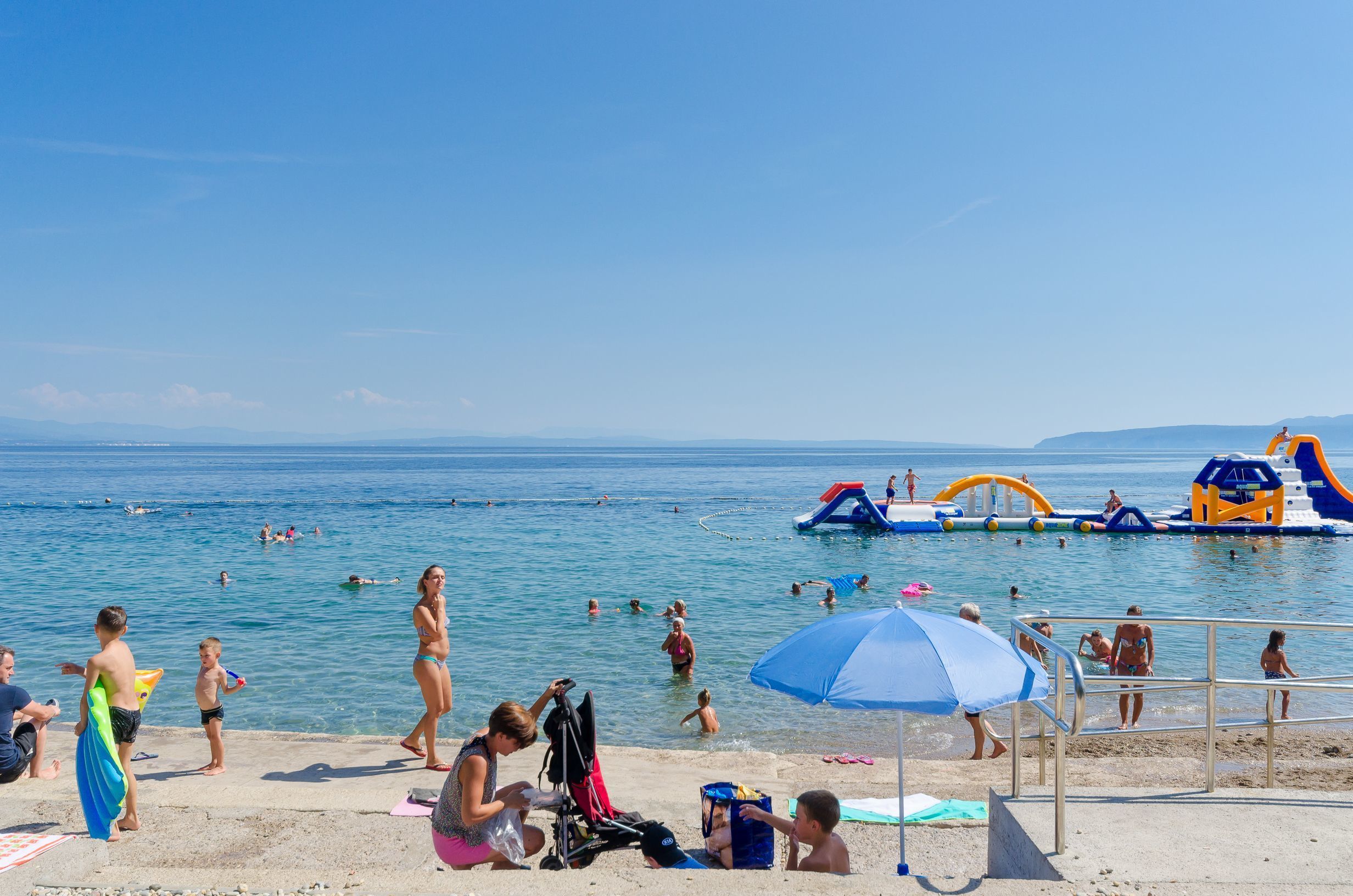 Una playa con gente nadando y jugando, un puesto de salvavidas y estructuras acuáticas inflables.
