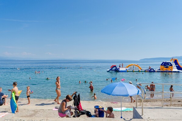 A beach with people swimming and playing, a lifeguard stand, and inflatable water play structures.