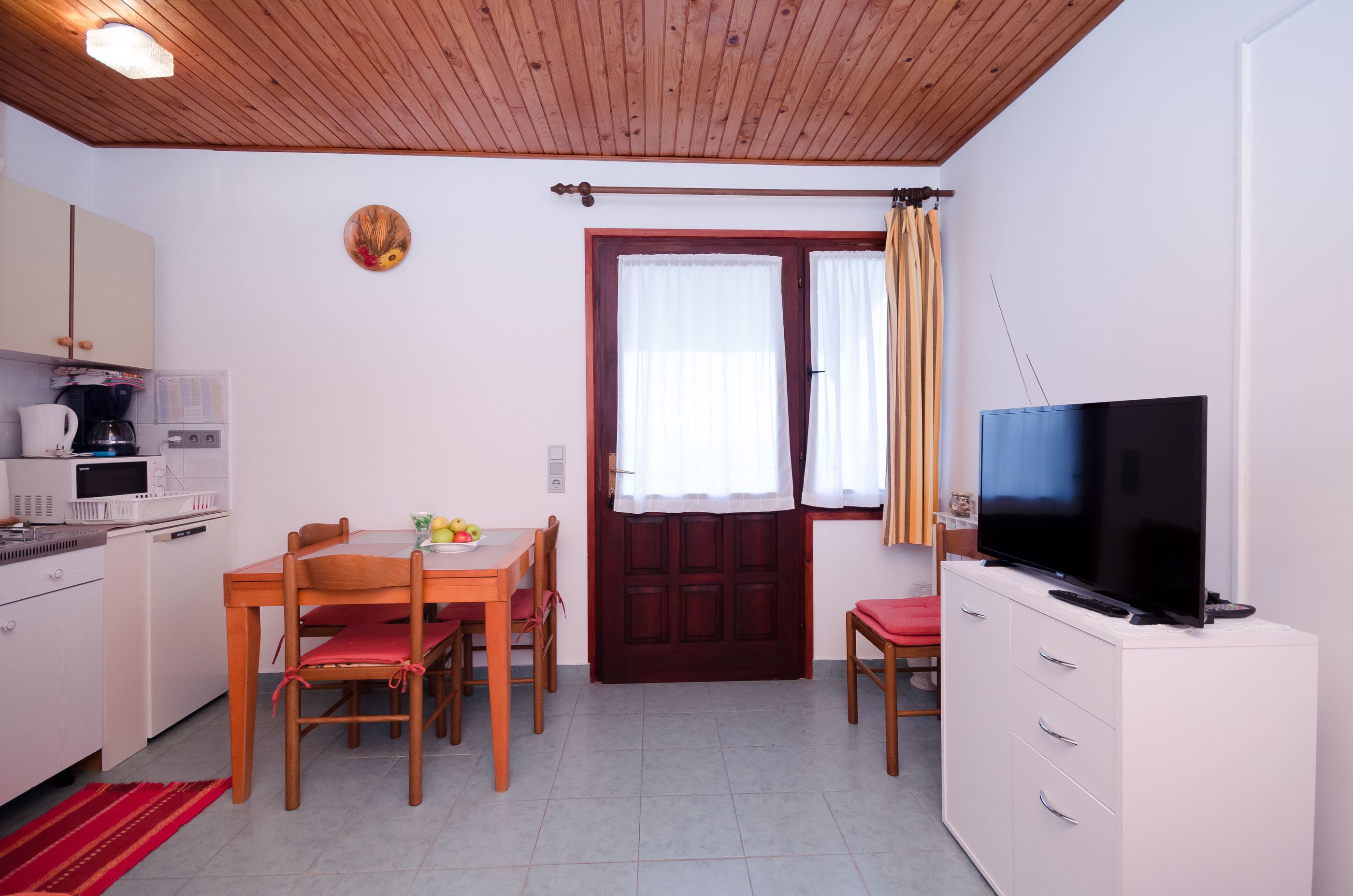 Una cocina compacta con comedor, televisor y techo de madera.
