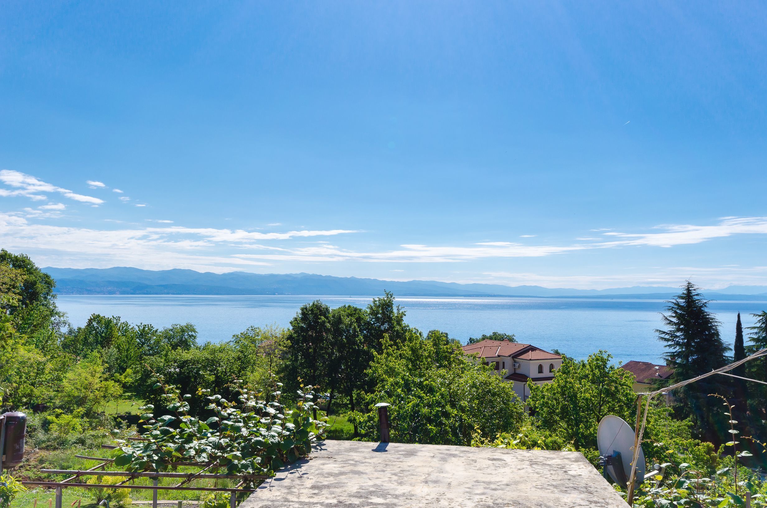A scenic view of a lake with mountains in the background, surrounded by lush greenery and a few houses.