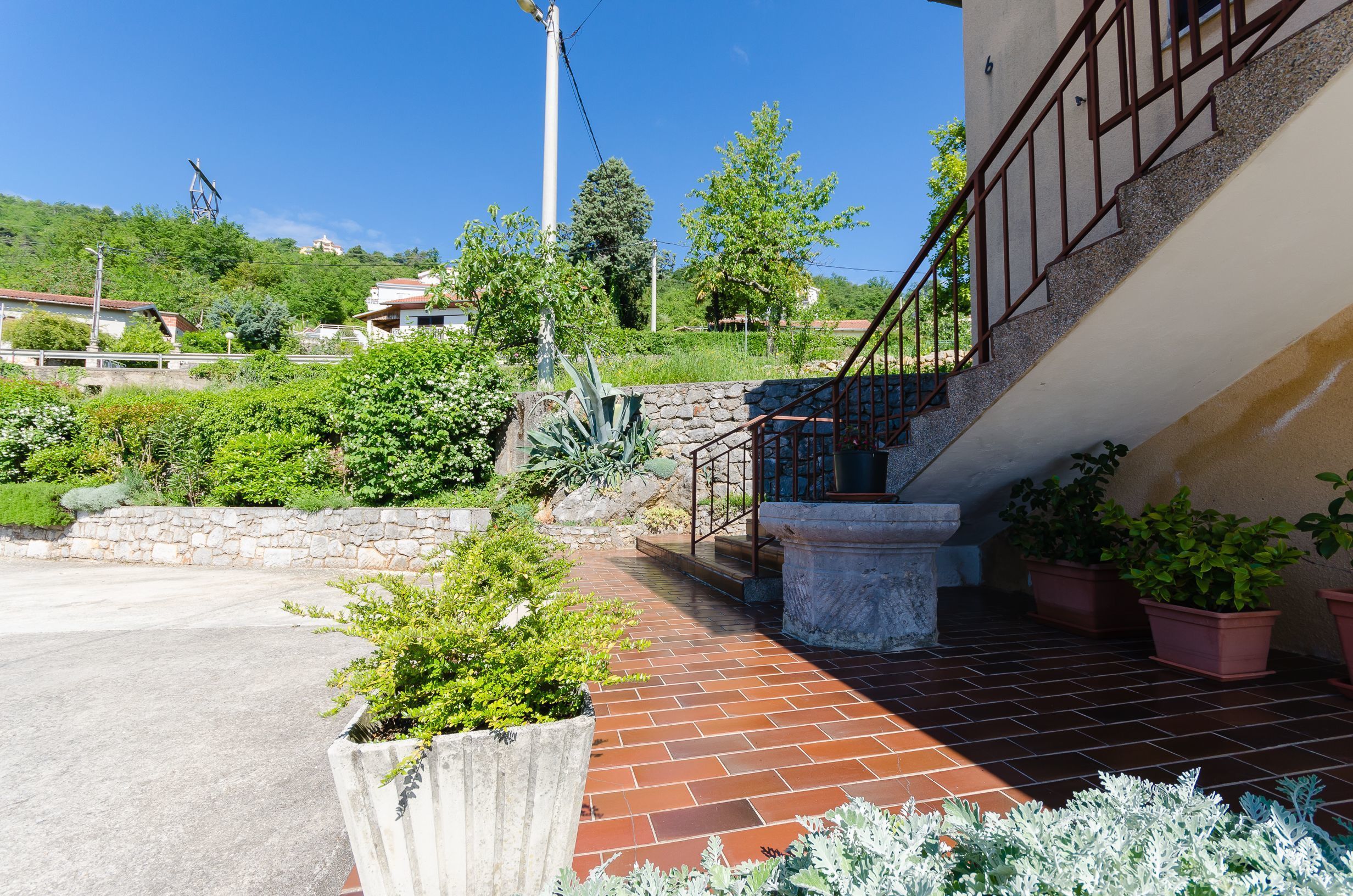 A residential area with a staircase leading to a second floor, surrounded by greenery and a clear sky.