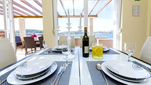 Une table à manger dressée avec des assiettes, des couverts et des verres, ainsi qu’une bouteille de vin et un pichet de limonade.