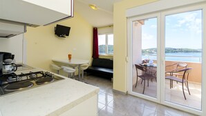 Une cuisine équipée d’une cuisinière à gaz, un coin repas avec une table et des chaises, un canapé et un balcon avec vue sur la mer.