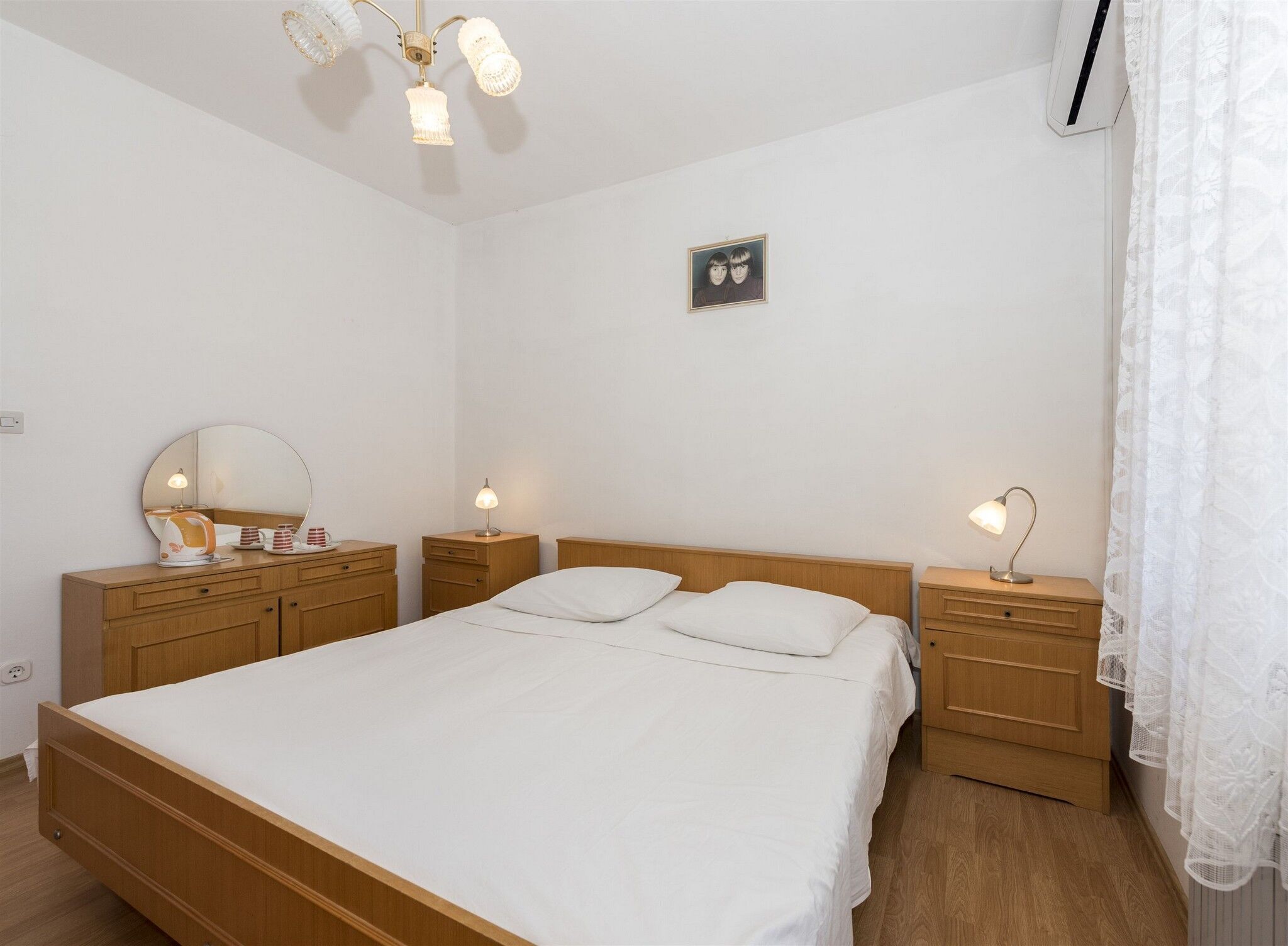 A bedroom with a wooden bed, bedside tables with lamps, a mirror, and a framed picture on the wall.