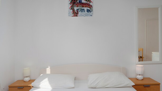 A neatly made bed with white linens and two pillows, flanked by wooden nightstands with lamps. - Apartments Family Gligora (Mandre)