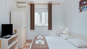 A hotel room with a bed, a TV, a wardrobe, and a window with curtains. - Apartments Family Gligora (Mandre)