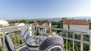Varanda com mesa, cadeiras e uma garrafa de vinho, com vista para uma paisagem deslumbrante com edifícios e céu claro.