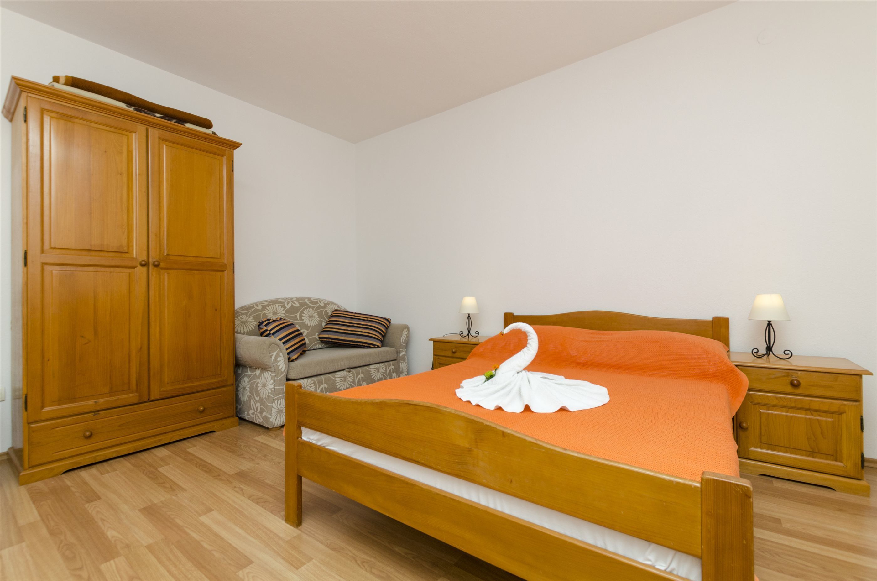 Un dormitorio con una cama de madera, un armario, un sofá y lámparas de noche.