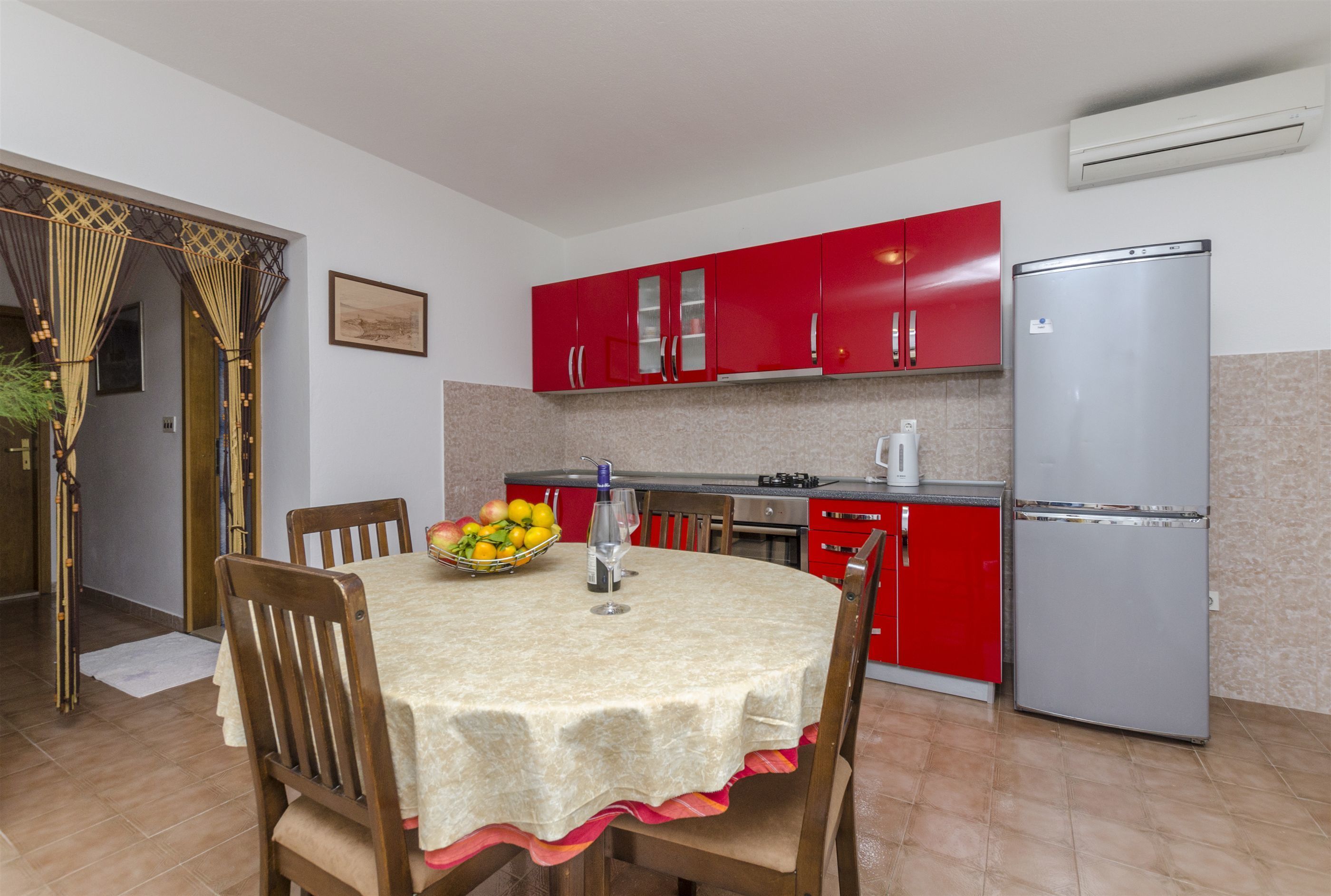 A kitchen with red cabinets, a stainless steel refrigerator, and a dining table with chairs.