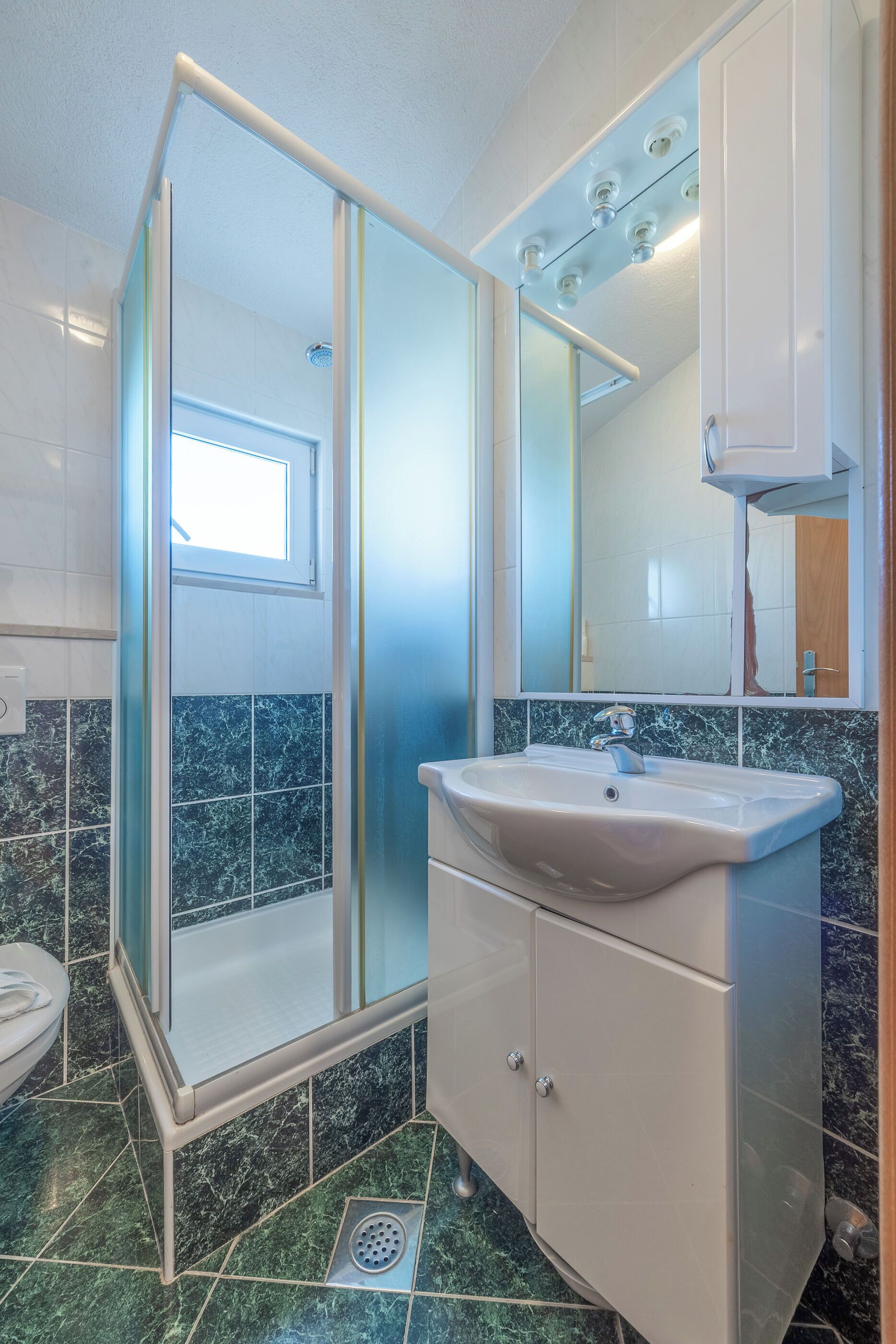 A bathroom with a glass shower enclosure, a sink with a mirror, and tiled walls.