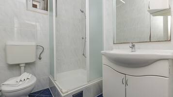 Un baño con inodoro, cabina de ducha y lavamanos con espejo.