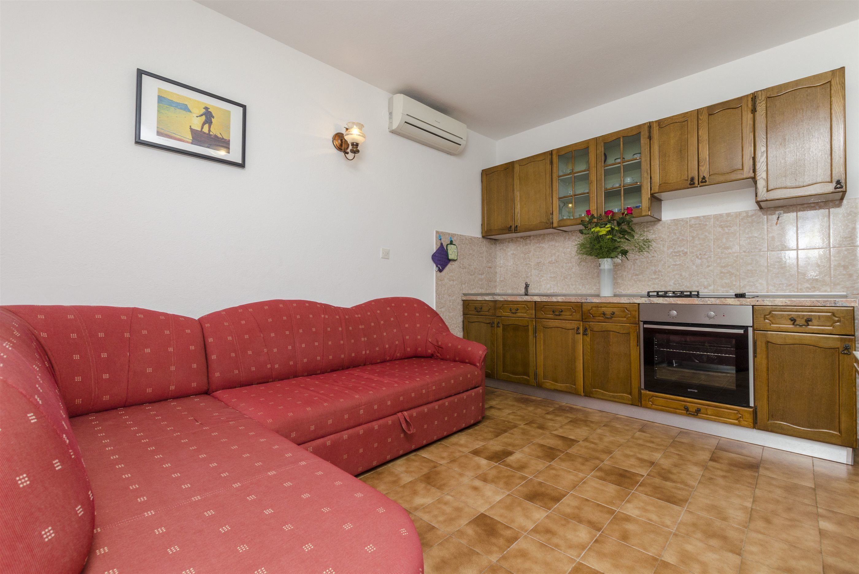 A kitchen with wooden cabinets, a built-in oven, and a red sofa.