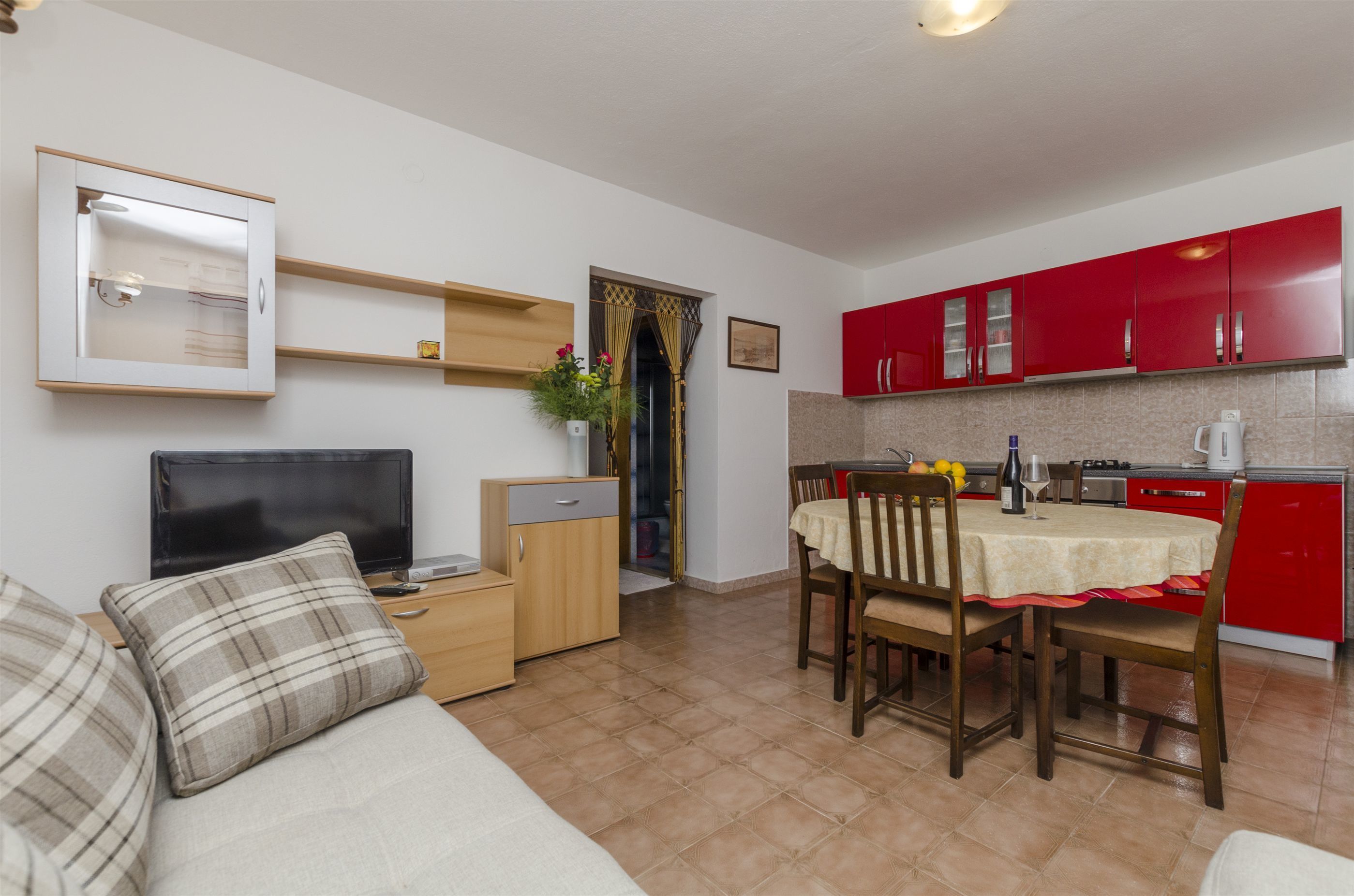 Un espacio habitable compacto con televisor, sofá, mesa de comedor y armarios de cocina rojos.