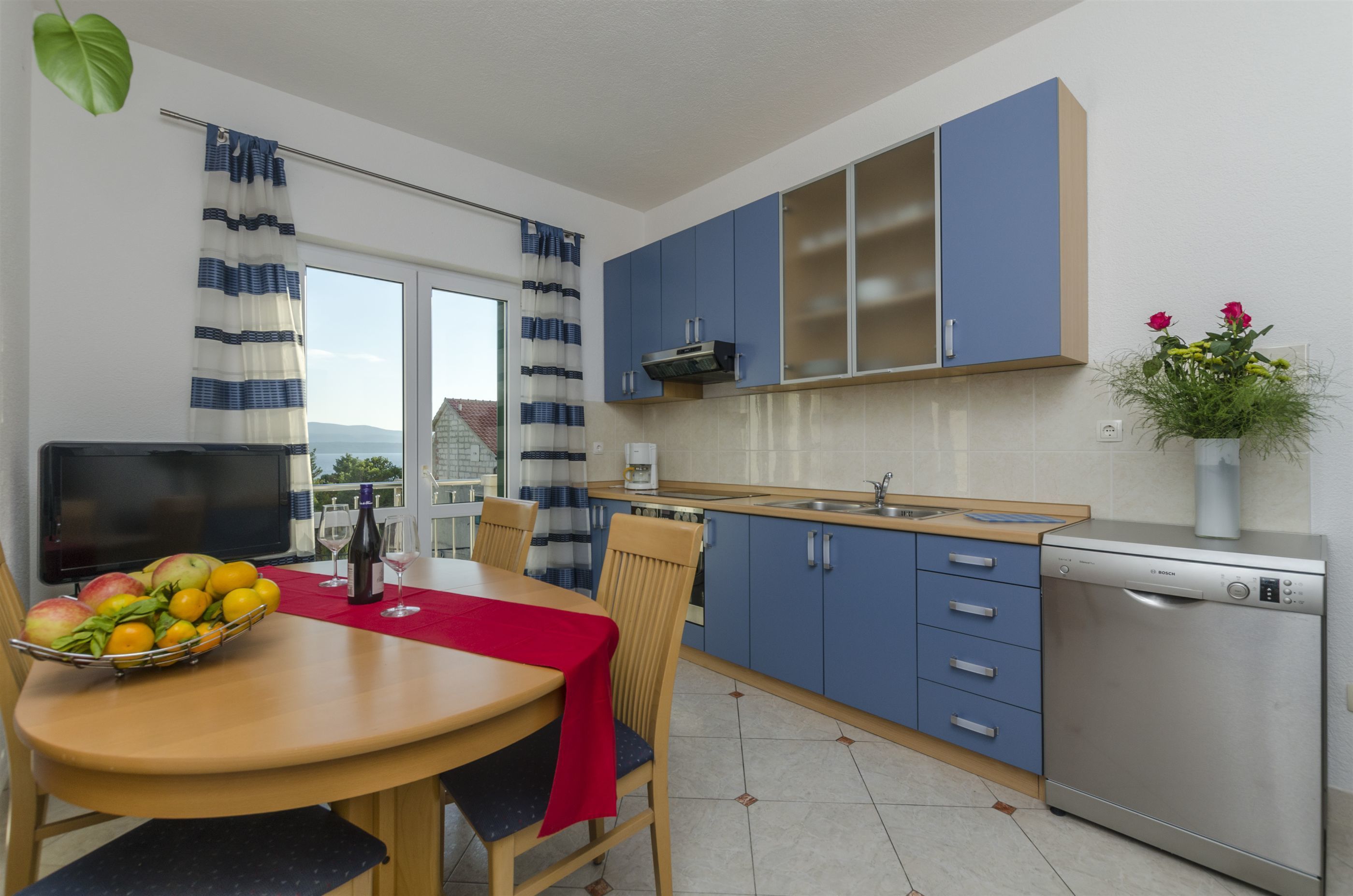 A modern kitchen with blue cabinets, a dishwasher, and a dining area with a table set for two.