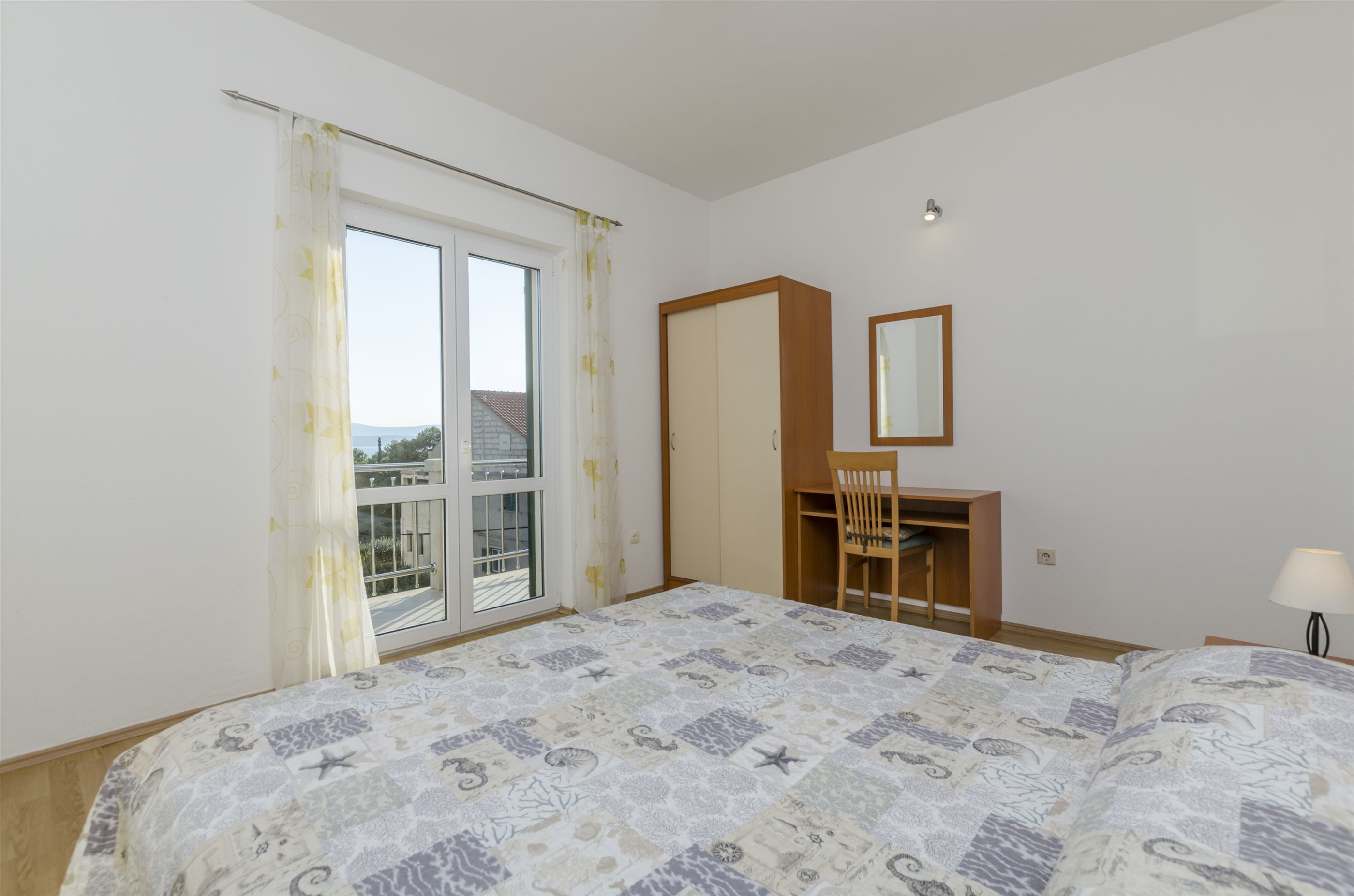Ein Schlafzimmer mit Bett, Schreibtisch, Stuhl, Kleiderschrank und einem Fenster mit Vorhängen.