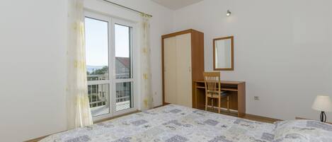 A bedroom with a bed, a desk, a chair, a wardrobe, and a window with curtains.