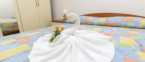 Una cama bien hecha con un edredón colorido, una toalla blanca con forma de cisne y una planta pequeña sobre la cama.