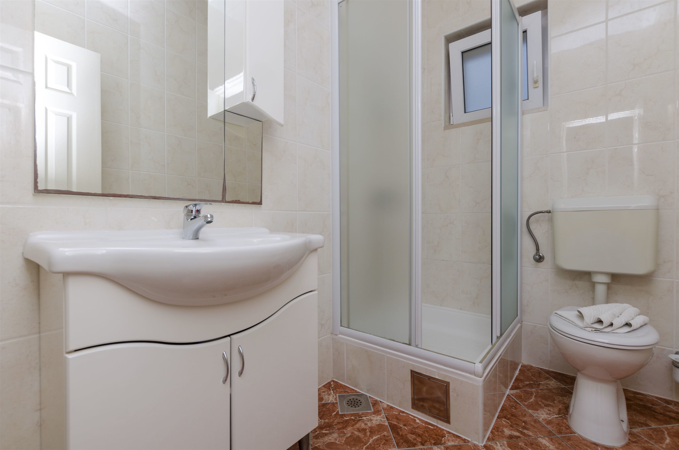 Een badkamer met een wastafel, spiegel, douche, toilet en betegelde wanden.